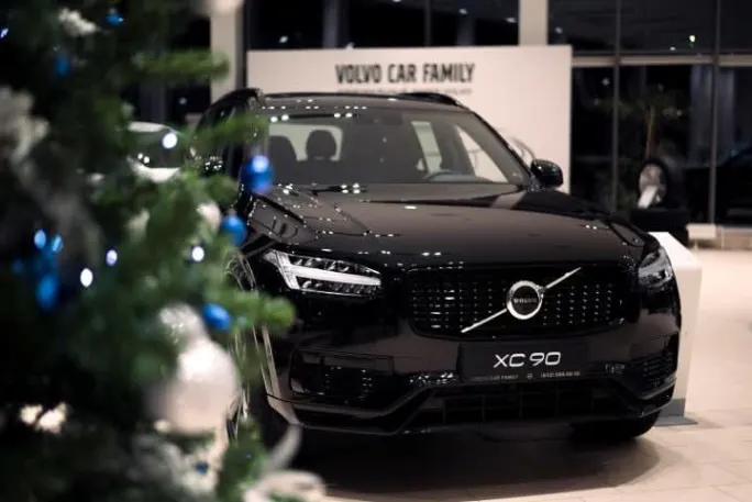 Black Volvo XC90 on display in a showroom with a Christmas tree nearby.