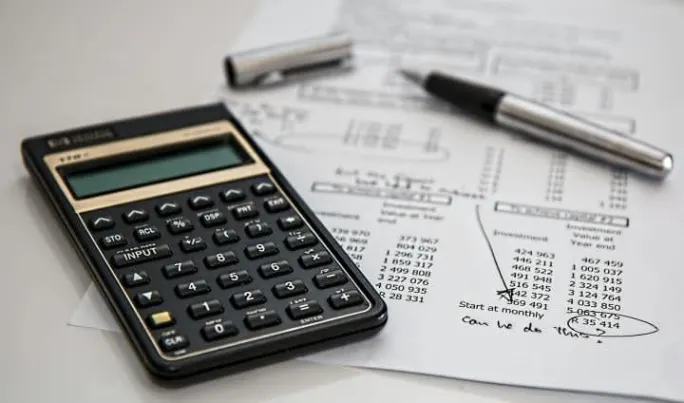 Calculator on top of printed financial documents with charts and numbers, with a pen and cap nearby.