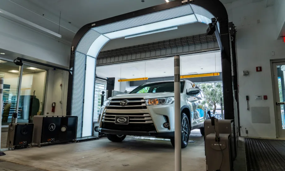 A white Toyota Highlander drives through a UVeye automated vehicle inspection system inside a dealership service area, part of Cox Automotive’s vAuto integration for faster appraisals.