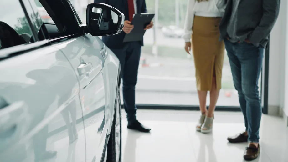 Couple talking with auto salesman next to new car inside dealership