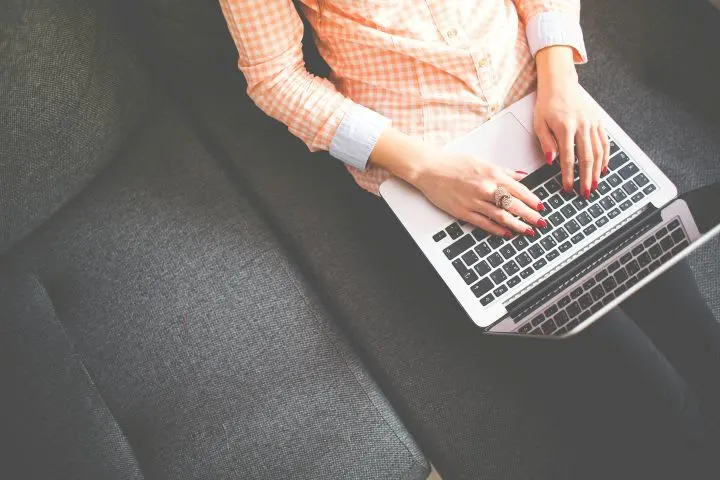 Photo of woman typing on a laptop as she sits on a couch