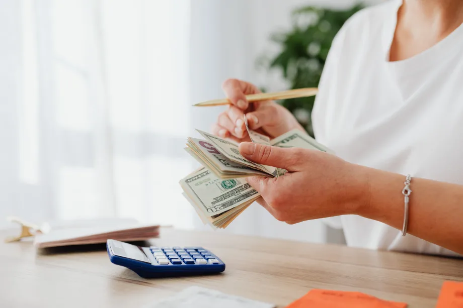 Photo of woman counting cash with a calculator sitting on a desk in front of her