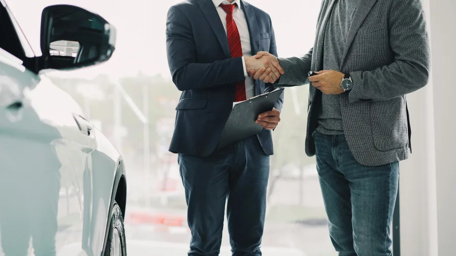 Photo of two businessmen shaking hands next to a white car in a showroom