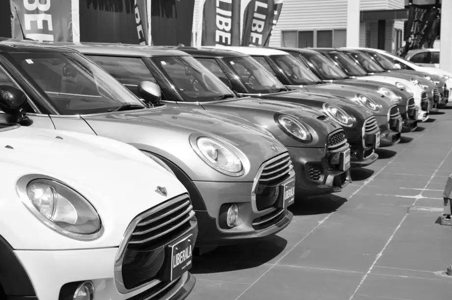 Gray-scale photo of a line of Mini cars in a dealership parking lot
