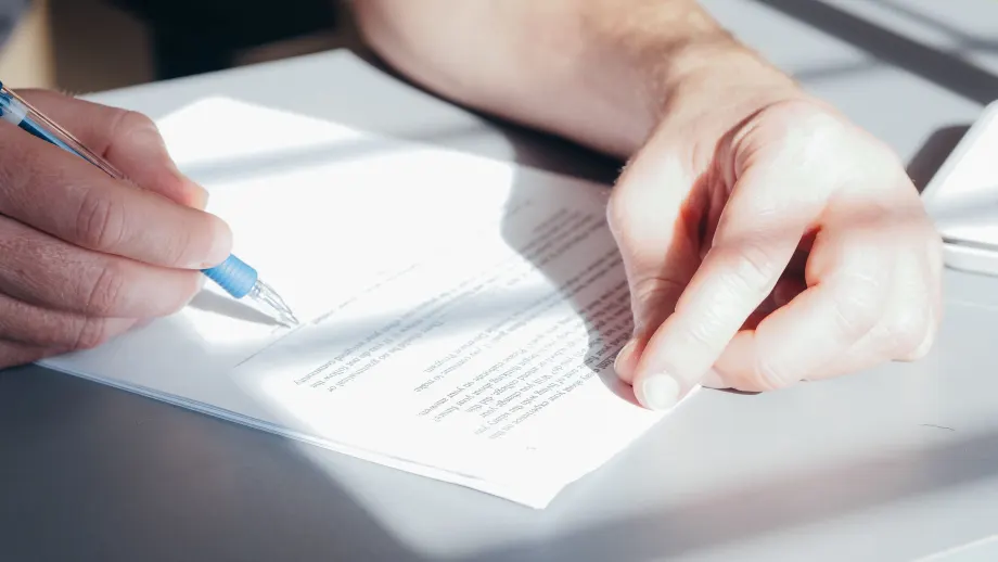 Photo of man signing document with a blue pen