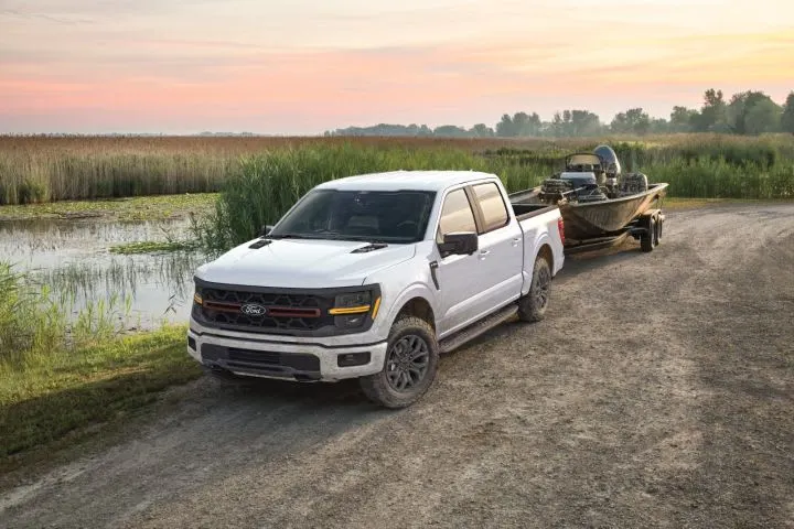 Photo of white Ford F-10 pickup parked on a dirtl road next to a body of water and with a fishing boat hitched to it