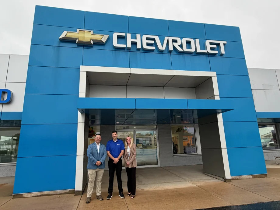 Two men and one woman standing in front of blue walled Chevrolet dealership entrance.