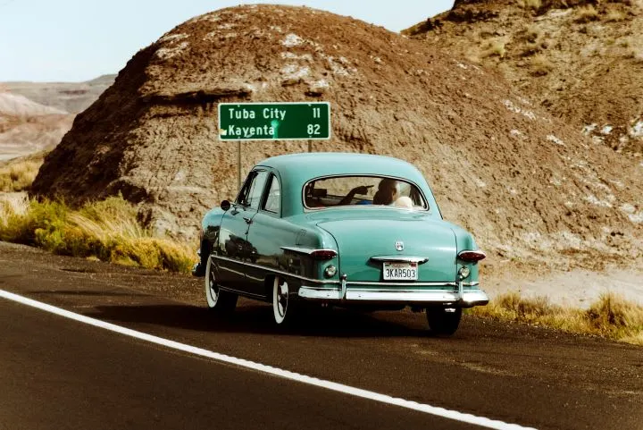 Teal antique car driving on road.