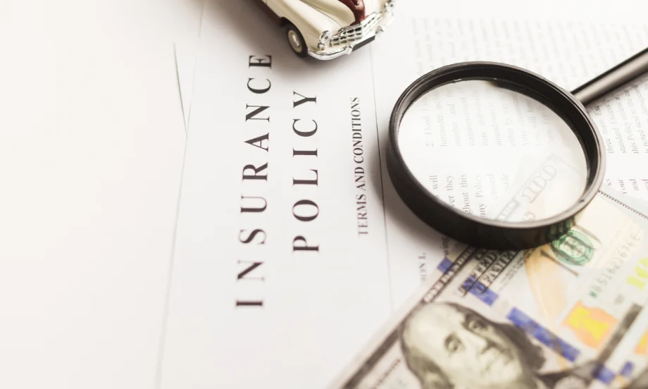 $100 bill and magnifying glass on top of paper that says insurance policy terms and conditions.
