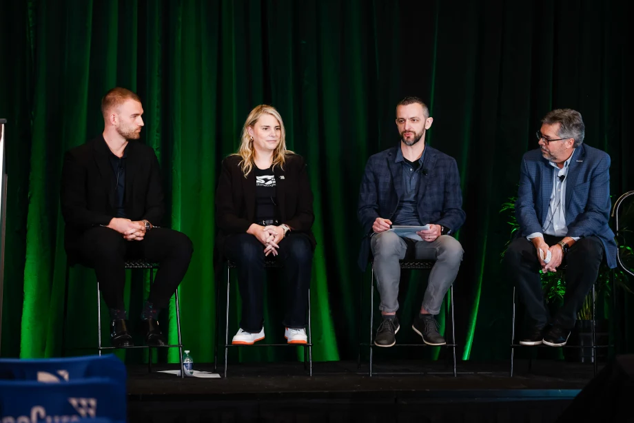 Three men and one woman sitting on a green backlit stage talking