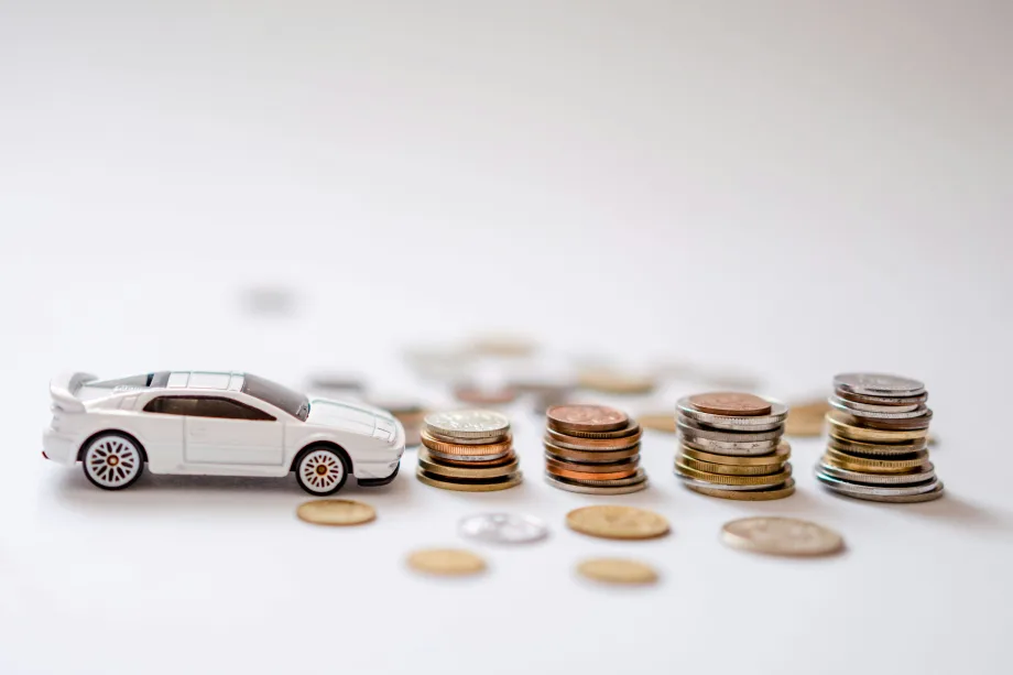 Tiny toy car in front of small stacks of coins