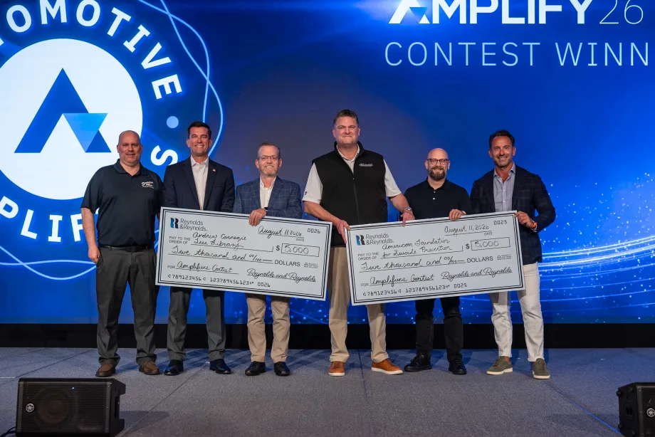 Six men standing on stage receiving two giant $5,000 checks.