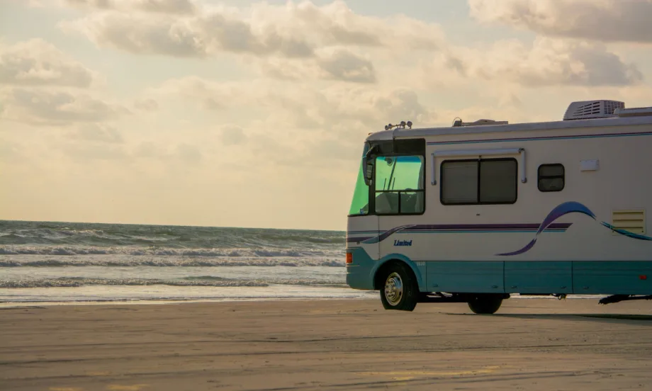 Blue and white RV parked on beach facing the ocean.