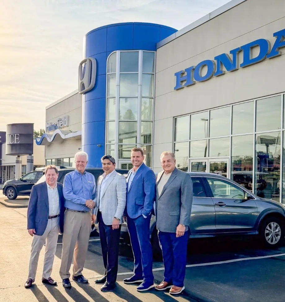Five men smiling for photo in front of Honda car dealership.