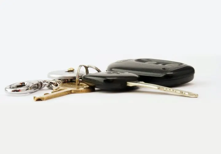 Photo of a keyring with mltiple keys, including a car key fob, on a white surface