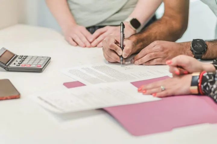 Three people's hands on desk as one signs a document
