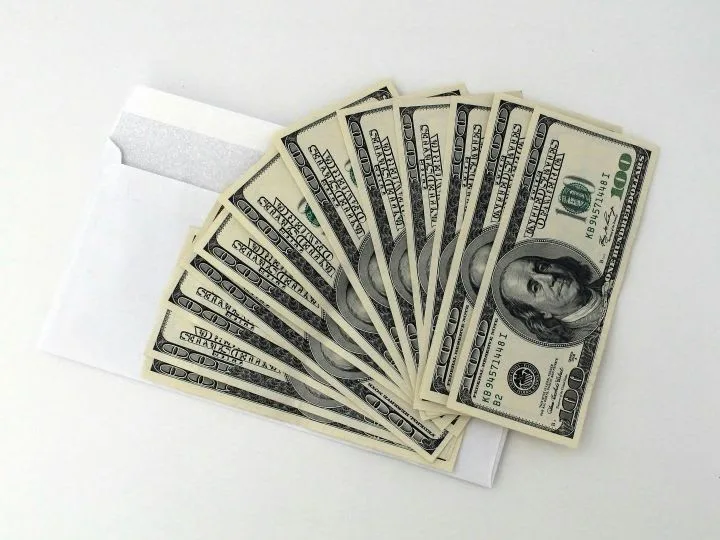 A fan of $100 bills sitting on a white envelope