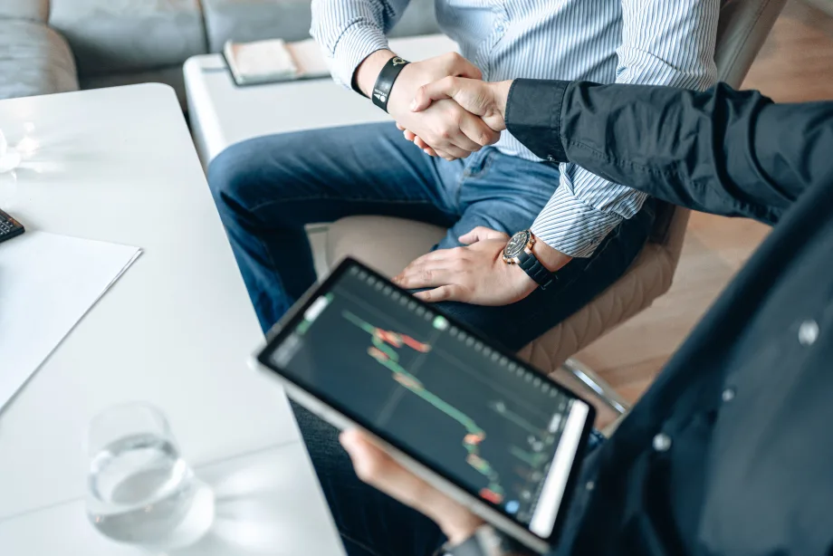Two businessmen shaking hands as one holds an electronic pad