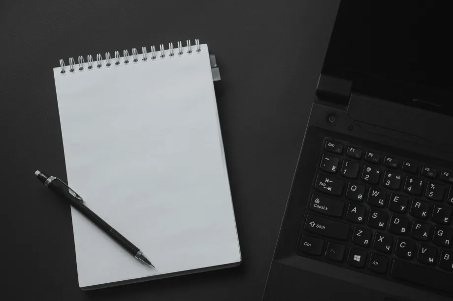 Photo of notepad and pen next to computer keyboard on desktop