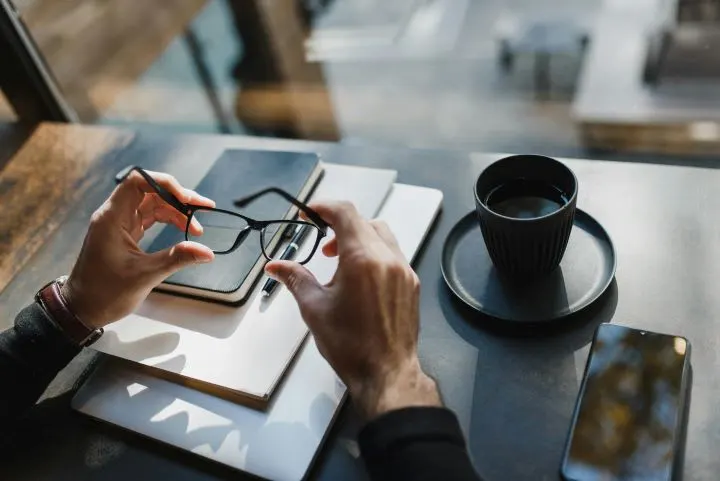 Photo of businessman's hands holding eyeglasses at a desk