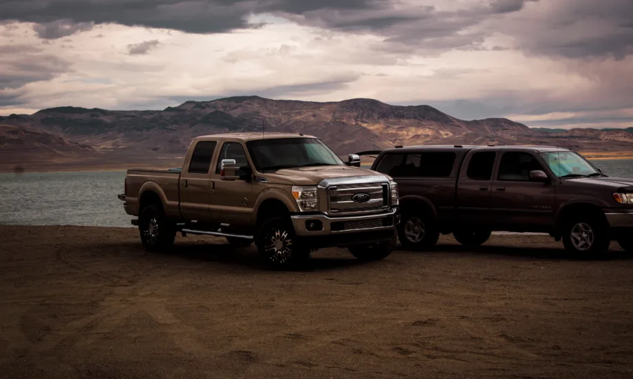 outside shot of two trucks in front of a body of water with a cloudy sky