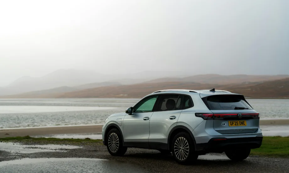 white SUV parked in front of a body of water with a gray sky background