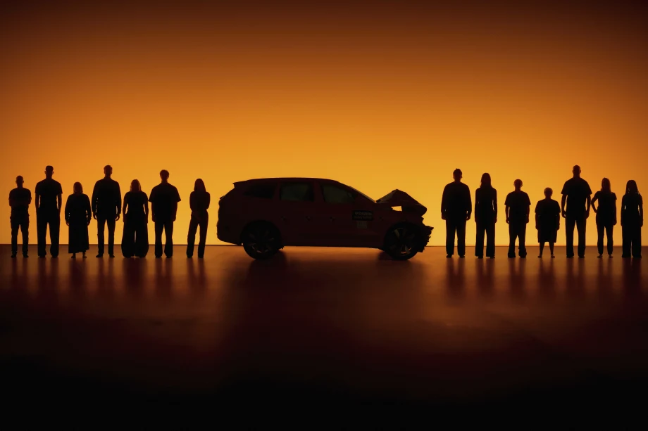 orange background behind a line of people with a crashed car in the middle