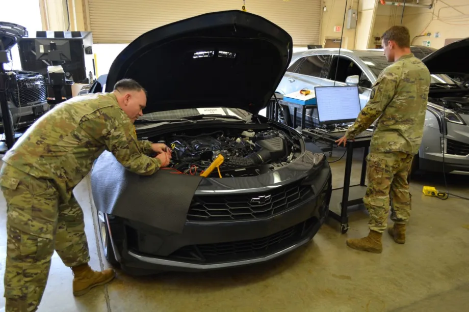 two men in Army uniforms looking under the hood of a car