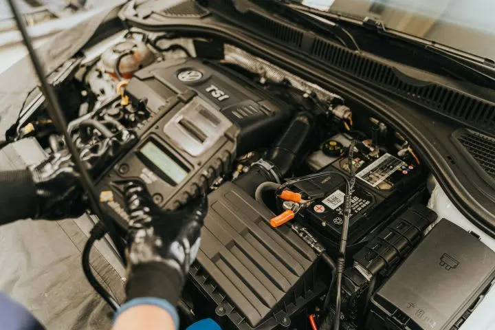 Mechanic holding a vehicle diagnostic device while standing above an open car hood