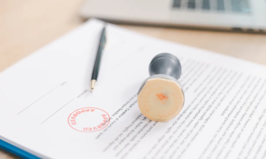 white document with black text, stamp laying on top with red circle stamp of approval on top of paper