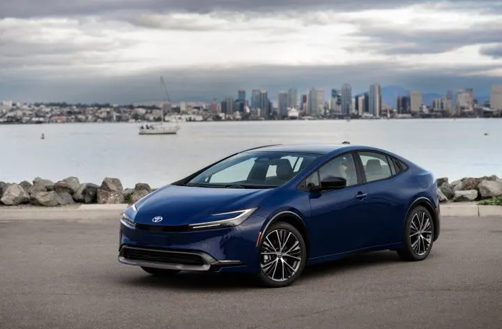Photo of blue Toyota Prius parked next to body of water with city skyline in background