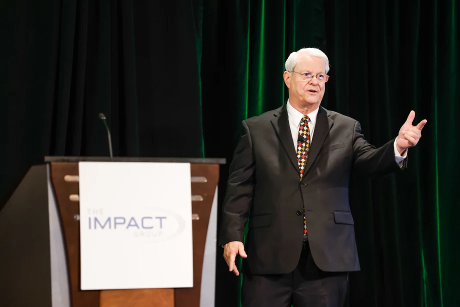 man with white hair and glasses delivering a speech standing next to a podium