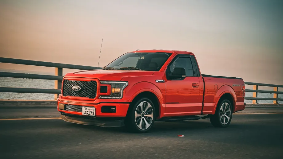 red pickup truck in front of railing and body of water with setting sun