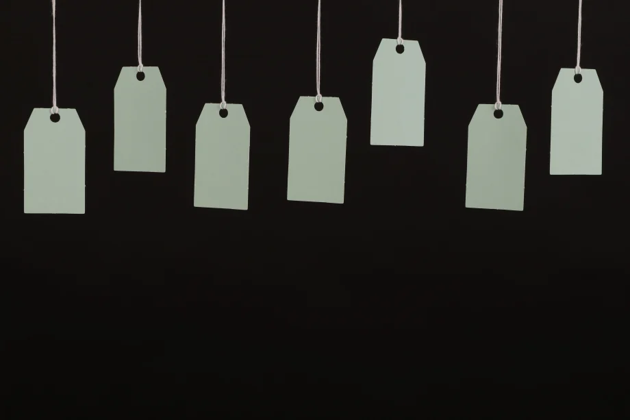 About half a dozen blank white tags hanging from above in front of a dark background