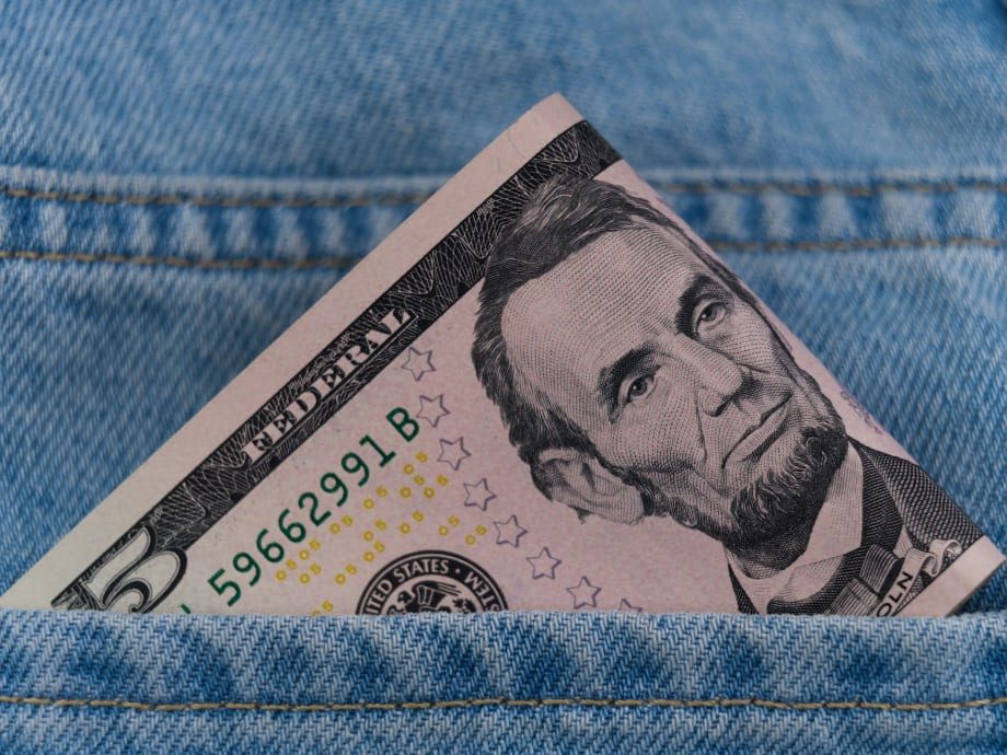 $5 bill poking out of blue jeans pocket