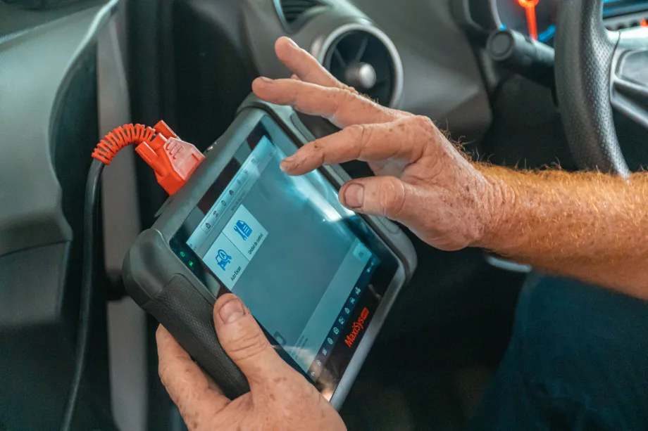 Mechanic's hand on digtial device screen next to a car