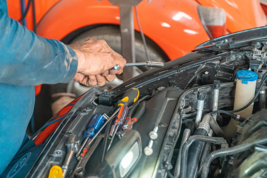 pair of hands holding tools working on a vehicle under the hood