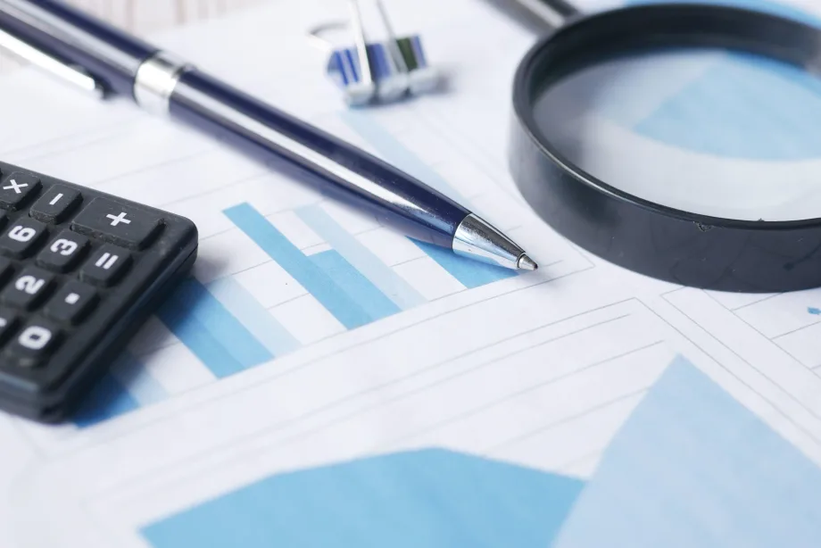 Photo of financial documents with a magnifying glass, calculator and pen on top